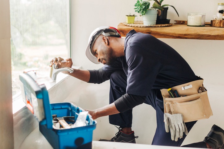 A plumber fixing a bathtub faucet with a toolbox nearby in Visalia, CA