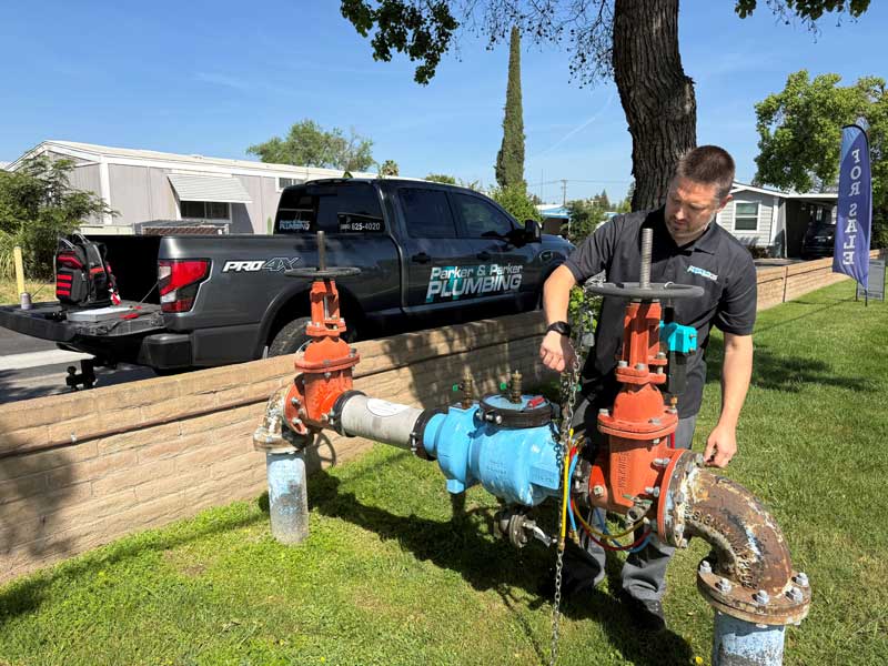 Plumber servicing outdoor water valve near service truck