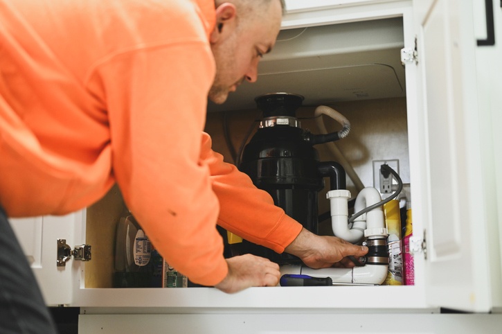 Technician repairing plumbing beneath a kitchen sink in Visalia, CA
